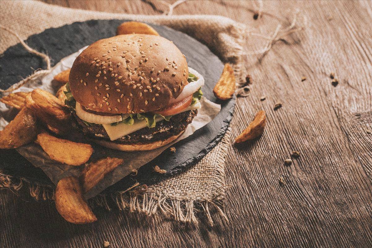 Ein Burger mit Pommes auf einem Holztisch serviert.