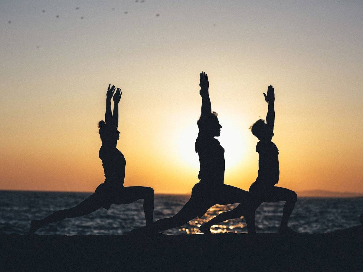 Drei Menschen in Yoga-Posen am Strand bei Sonnenuntergang.