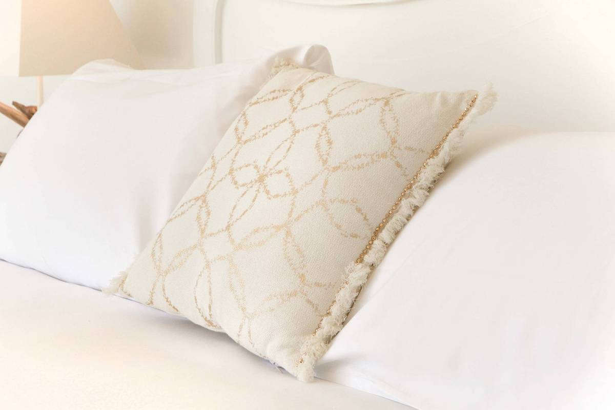 Ein weißes Kissen mit goldenen Mustern auf einem weißen Bett