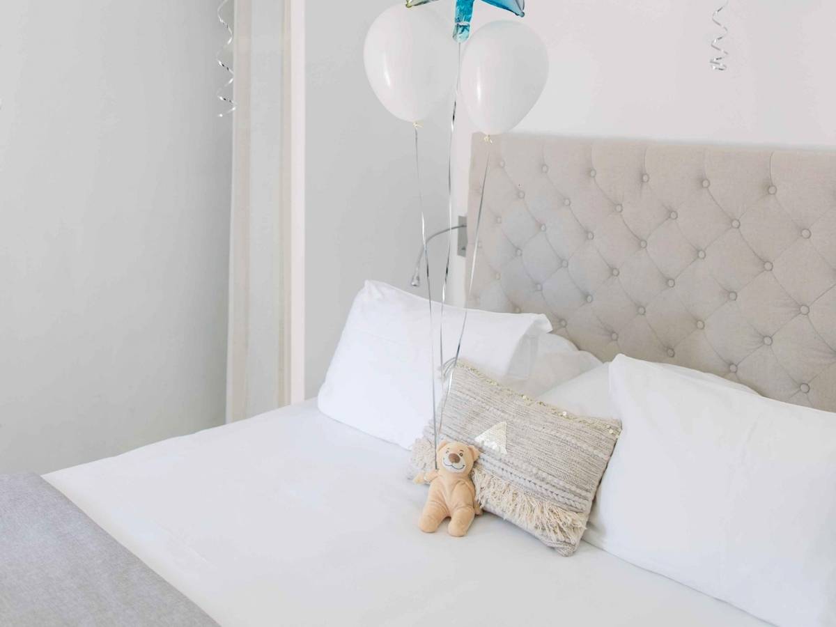 Ein Bett mit weißen Kissen und Ballons, darunter ein Teddybär auf einem gemusterten Kissen.
