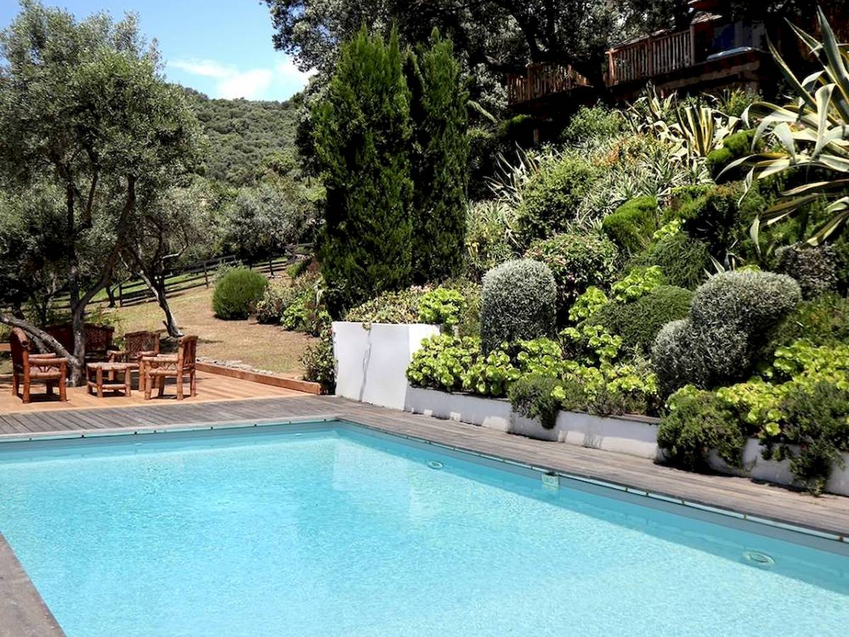 Außenbereich des L'Hostellerie du Moulin Hotels mit Swimmingpool, Holzmöbeln und umliegenden Gärten.