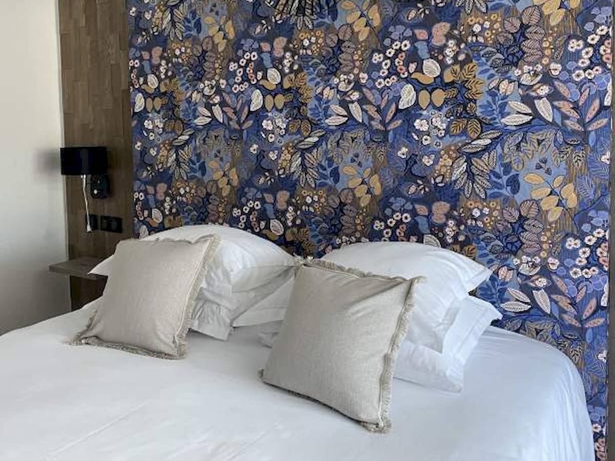 Ein Bett mit weißen Laken und Kissen vor einer blauen Blumentapete im Hotel La Lagune.