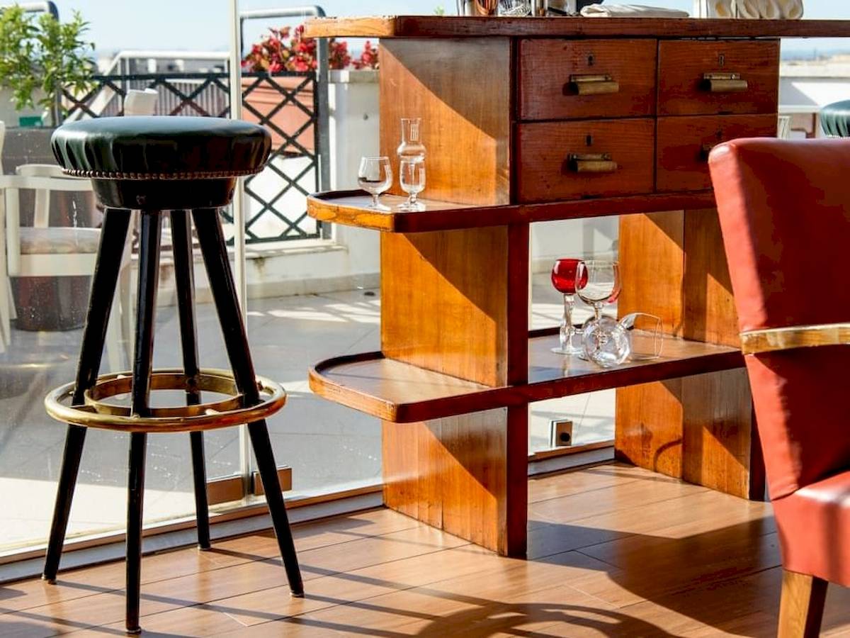 Foto von Möbeln auf der Terrasse des Bettoja Hotel Mediterraneo mit einem Barstuhl und einem Barwagen mit Gläsern.