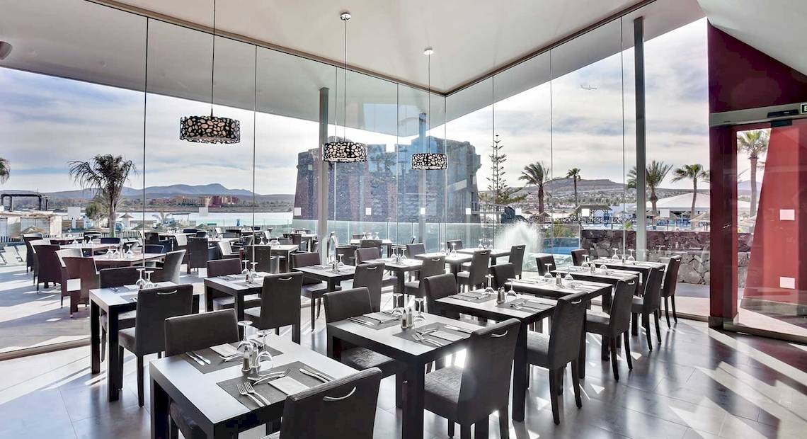 Innenbereich des Barcelo Fuerteventura Castillo Hotel mit großen Glaswänden und Blick auf die Stadt.