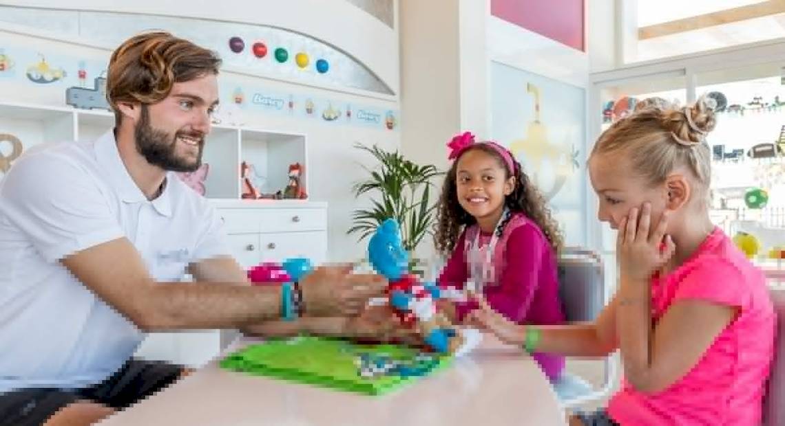 Ein Mitarbeiter des Barcelo Fuerteventura Castillo Hotels spielt mit zwei Kindern an einem Tisch.