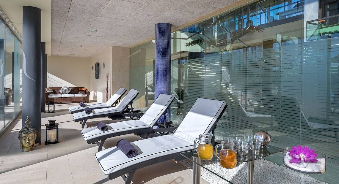 Innenbereich des Barcelo Fuerteventura Castillo Spa mit mehreren weißen Liegen, Glaselementen und einem Buddha-Dekor.