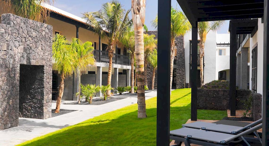 Außenbereich des Barcelo Fuerteventura Castillo Hotels mit gepflegtem Rasen, Steinwänden und Palmen.