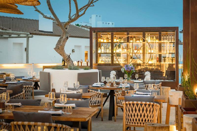 Außenbereich des Restaurants im Lago Resort Menorca - Suites del Lago mit beleuchteten Flaschen und Tischen.