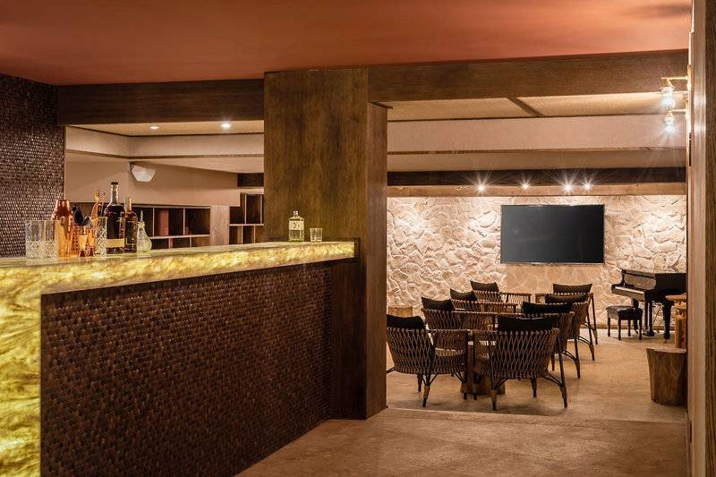 Die Bar des Lago Resort Menorca - Suites del Lago mit einer Theke, Möbeln und einer Fernsehwand.