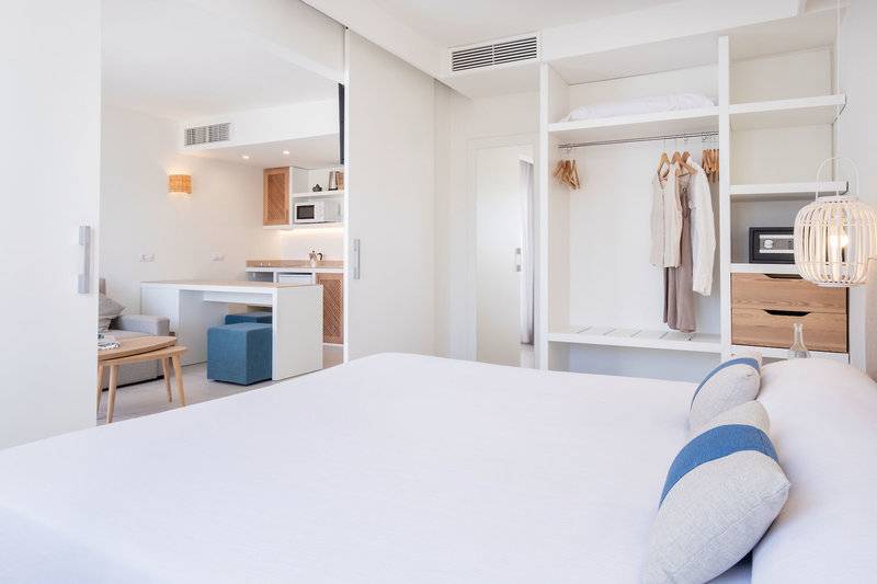 Innenansicht eines Zimmers im Carema Beach Menorca Hotel mit Bett, Kleiderschrank und Miniküche.