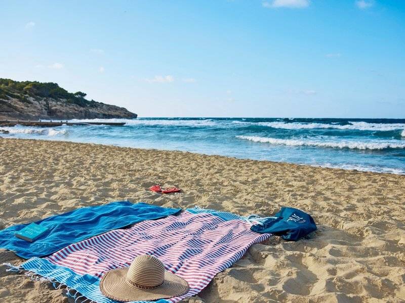 Ein Sonnenstrand mit blauen und roten Handtüchern, einem Buch und einem Hut.