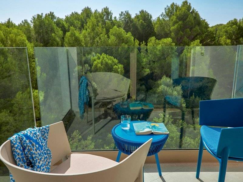 Balkon mit Aussicht auf Wald, blauen Stühlen und einem runden Tisch mit Buch
