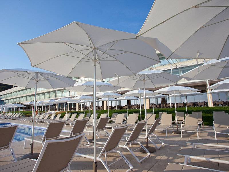 Poolbereich des Seth 55 Santo Tomás Hotels mit vielen weißen Sonnenschirmen und Liegestühlen.