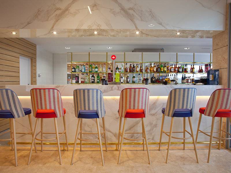 Innenansicht der Bar des Hotels Seth 55 Santo Tomás mit sechs bunten Barhockern und einer Theke mit vielen alkoholischen Getränken.