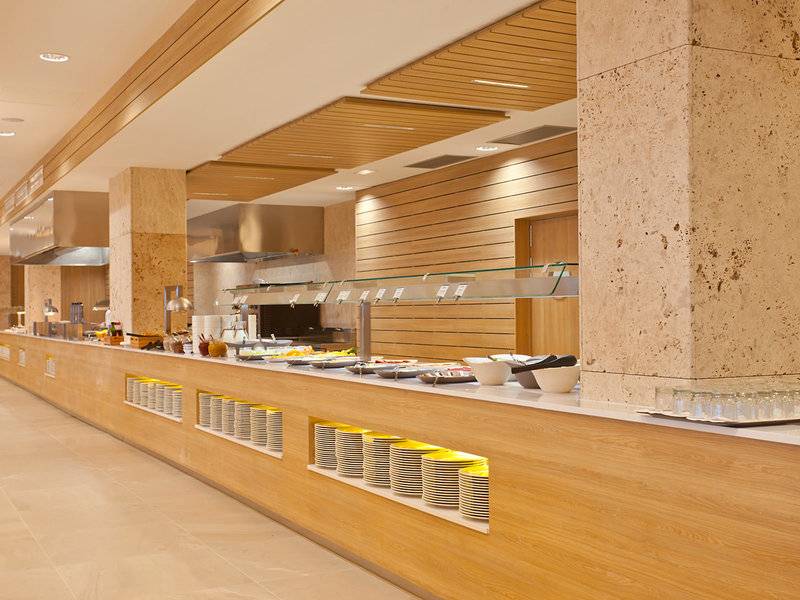 Buffetbereich des Seth 55 Santo Tomás Hotels mit Holzsäulen und einer Glastheke voller Speisen.
