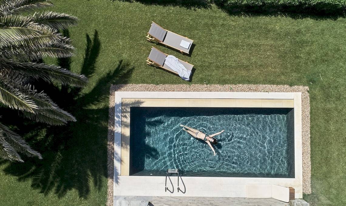 Aus der Vogelperspektive einer Frau, die im Schwimmbad schwimmt, mit Liegestühlen und Palmen.