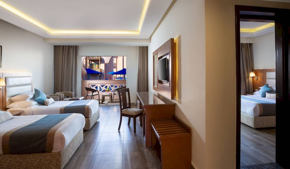 Innenansicht eines Hotelzimmers im Pickalbatros Aqua Park Resort in Hurghada mit drei Betten, Schreibtisch und Fernseher.