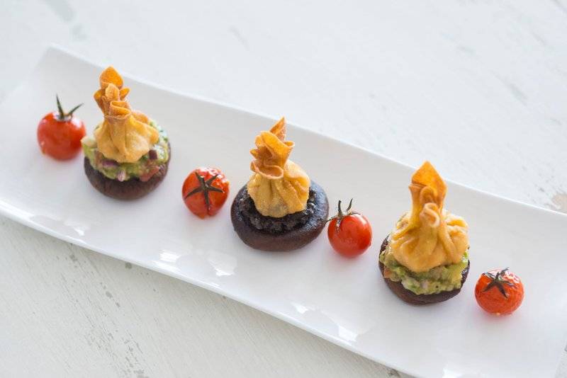 Fünf gebackene Champignons mit Avocadocreme und Tomaten auf weißem Teller