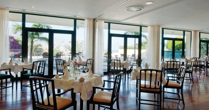 Innenansicht des Restaurants im Madeira Panorâmico Hotel mit vielen gedeckten Tischen und Fenstern.