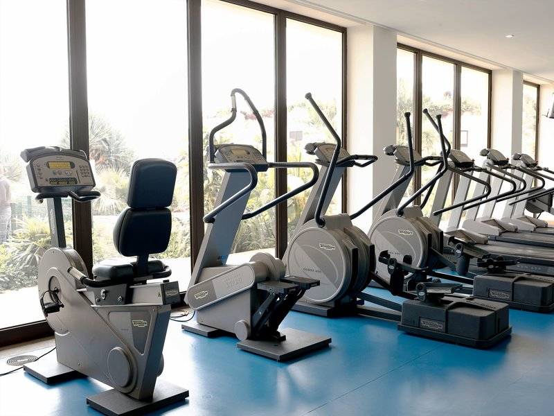 Fitnessgeräte im Hotel Porto Mare - PortoBay, in einer Reihe aufgestellt und vor großen Fenstern.