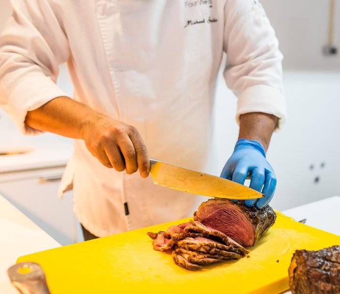 Koch schneidet Fleisch auf einem gelben Schneidebrett im Views Oasis Hotel