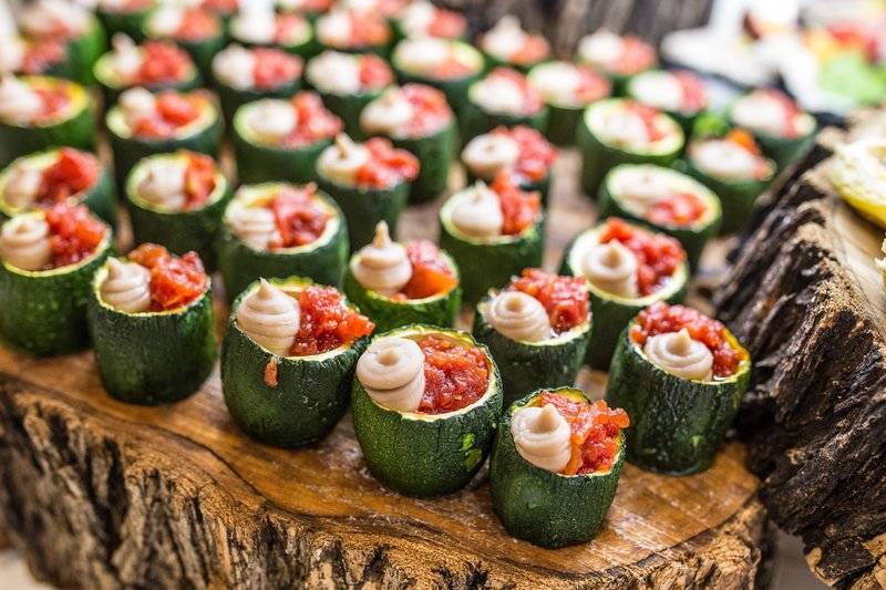 Nahaufnahme von grünen Zucchini-Tarteletts gefüllt mit einer roten Tomatenfüllung auf einem Holztisch.