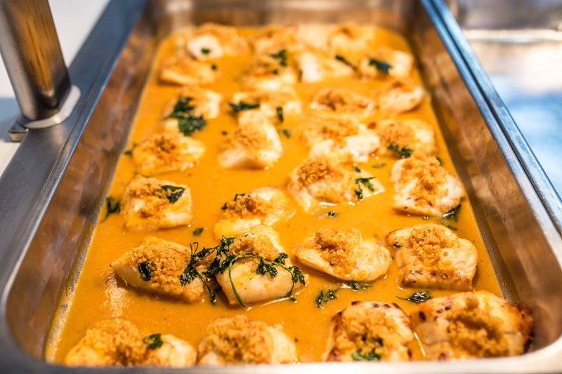Gebratene Jakobsmuscheln in einer goldbraunen Sauce, serviert in einer silbernen Speisekammer.