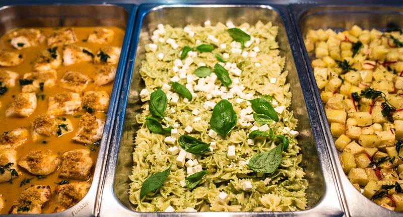 Buffet-Tisch mit verschiedenen Gerichten vom Views Oasis Hotel, darunter gebratenes Hähnchen, grüne Pasta mit Feta und Spinat sowie Kartoffelbeilage.