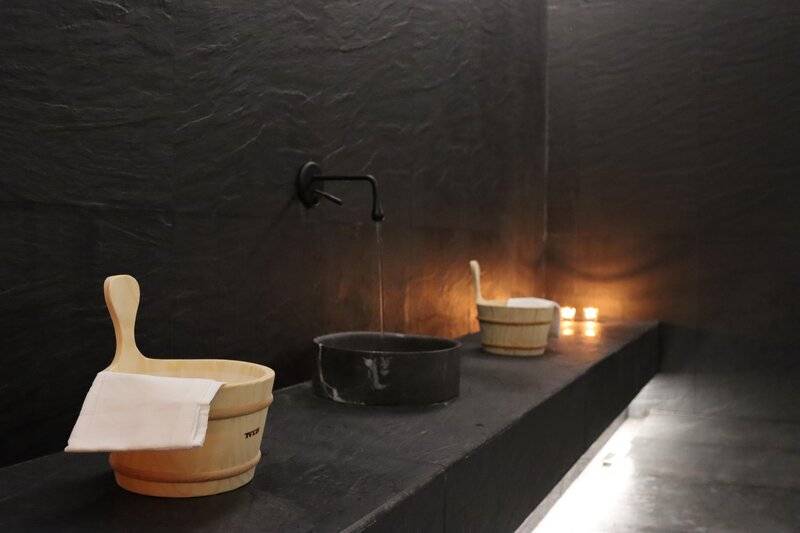 Ansicht des Badezimmers im Views Oasis Hotel mit schwarzen Wänden, Wassereimere, Handtuch und Lichtern.
