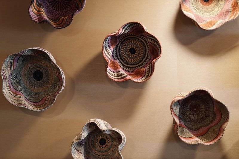 Fünf bunte geflochtene Körbe mit Blumenmustern auf einer beigefarbenen Oberfläche.