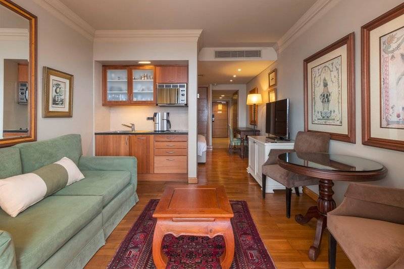 Wohnbereich der Suite im Royal Savoy Hotel mit grünem Sofa, Holztisch und Fernseher.