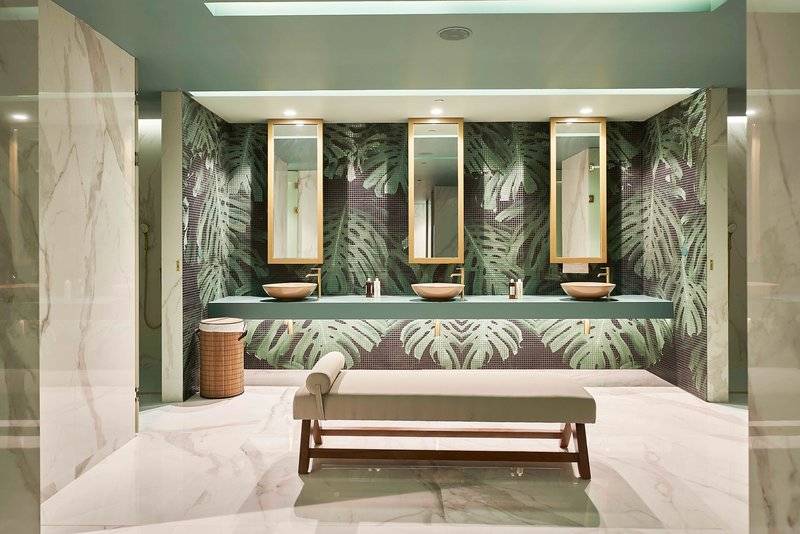 Badezimmer des Savoy Palace mit grüner Palmblatt-Tapete und drei Waschbecken.