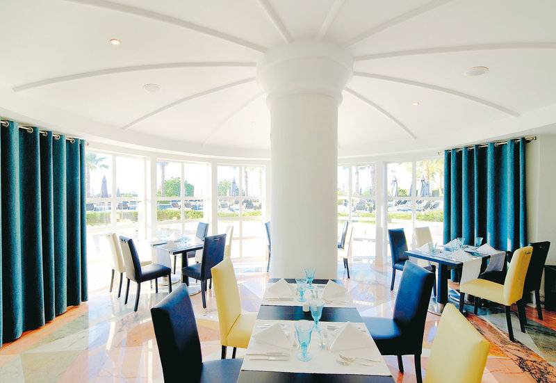 Innenansicht des Restaurants im Vila Galé Cerro Alagoa Hotel mit blauen Vorhängen und großen Fenstern.