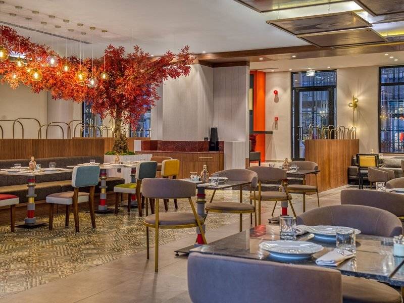 Innenansicht des Restaurants im Rixos Premium Belek mit bunten Stühlen und Tischen, einer roten Pflanze und moderner Einrichtung.