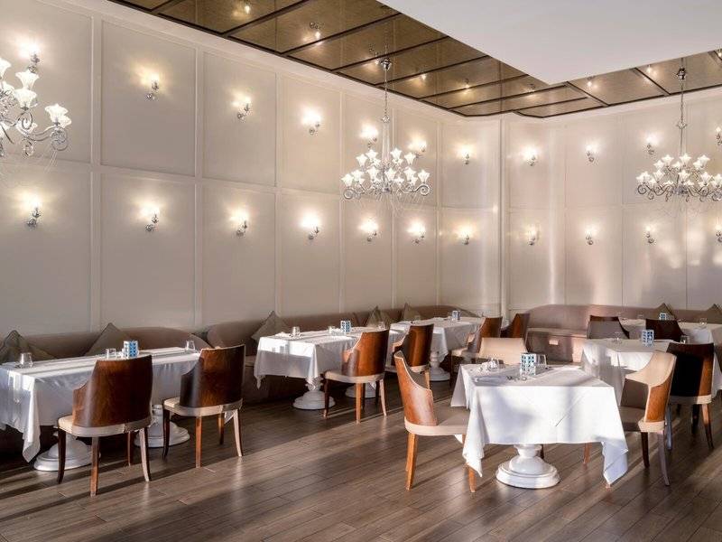 Innenansicht des Rixos Premium Belek Restaurants mit weißen Tischen, Holzboden und Kronleuchtern.