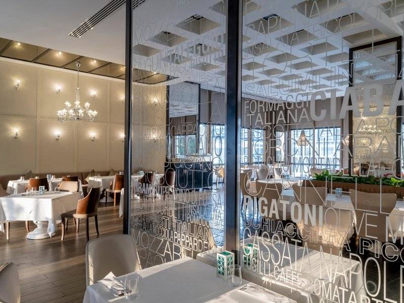 Innenansicht des Restaurants im Rixos Premium Belek mit Tisch, Stühlen und Glaswänden.