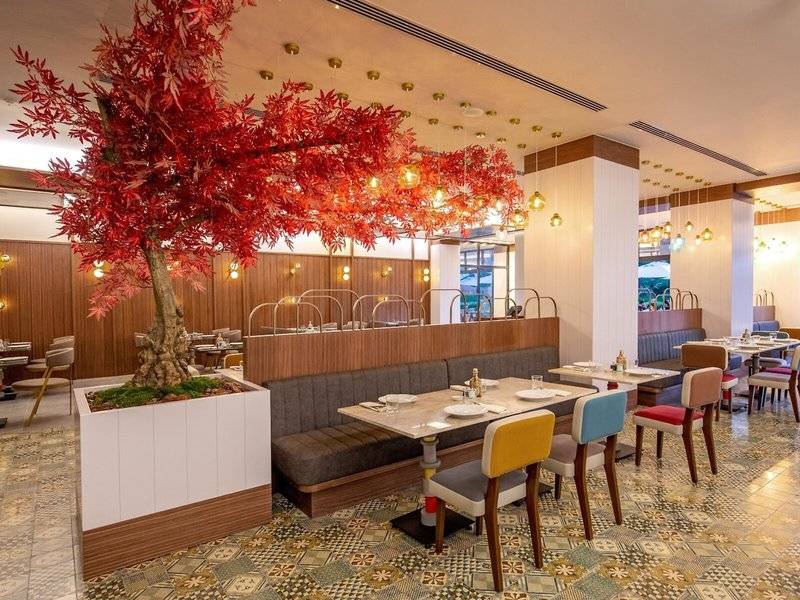 Innenansicht des Rixos Premium Belek Restaurants mit Tisch, Stühlen und rotem Baum