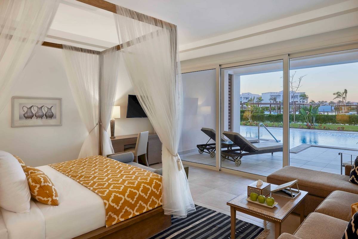 Schlafzimmer im Steigenberger Resort Alaya mit Baldachin-Bett, Swimmingpool und Terrasse im Hintergrund.