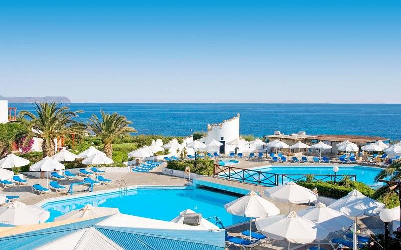 Außenbereich des Mitsis Cretan Village Resorts mit Swimmingpools, Sonnenliegen und Sonnenschirmen.