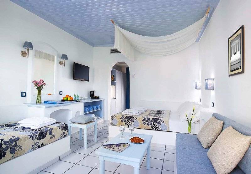 Innenansicht eines Zimmers im Mitsis Cretan Village Hotel mit zwei Betten, einem Sofa, einer Couch und einem Tisch.