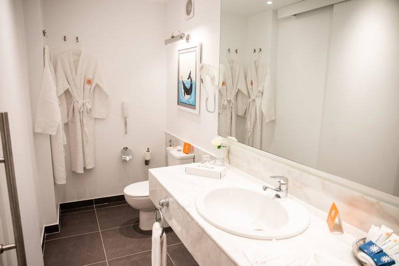 Badezimmer im Desert Rose Resort mit weißem Waschbecken, Spiegel und Robes an der Wand.