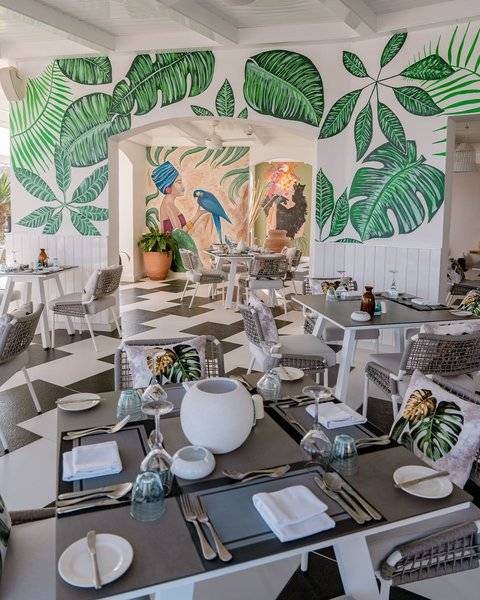 Innenbereich des Restaurants im Fort Arabesque Resort, Spa & Villas mit grünen Blattmalereien an den Wänden und einem schwarzen und weißen Schachbrettboden.