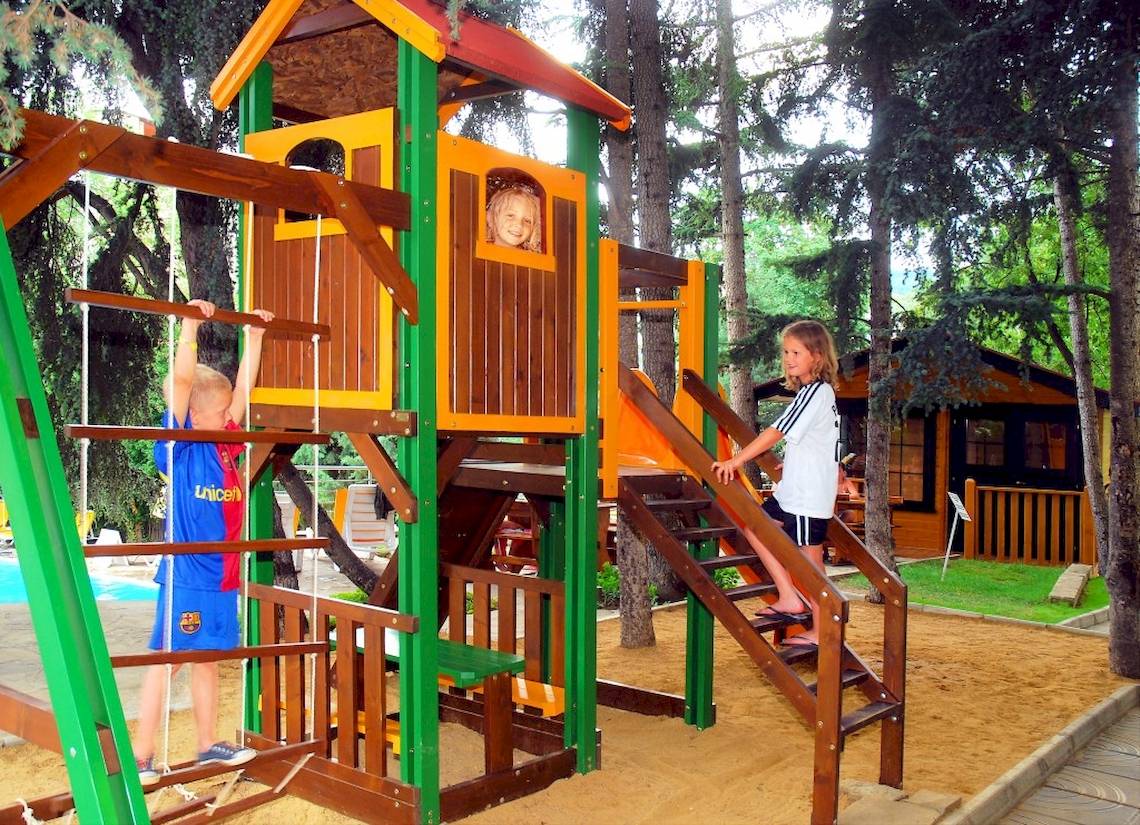 Ein Kinderspielplatz mit einer Rutsche und Klettergerüst im Wald mit drei Kindern, die spielen.
