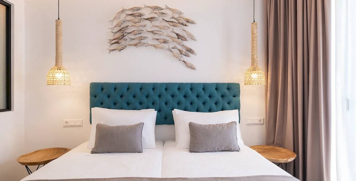 Schlafzimmer im Kalidon Panorama Hotel mit blauem Kopfteil, weißen Kissen und hängenden Lampen.