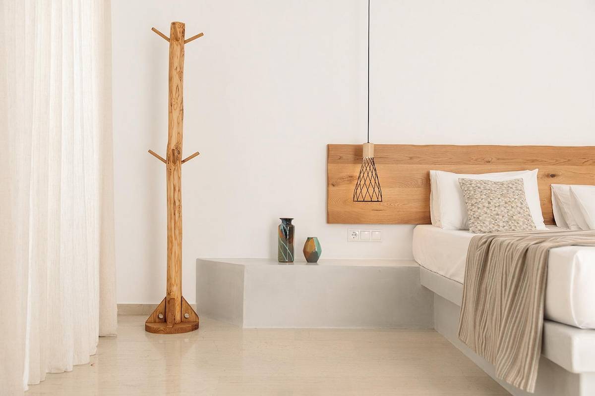 Ein modernes Schlafzimmer im Proteas Hotel mit weißem Bett, Holzkopfteil, Holzständer und weißen Wänden.