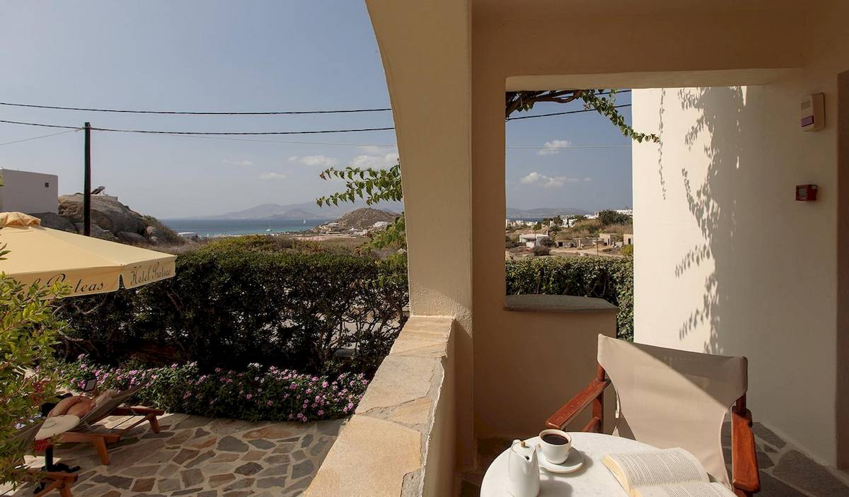 Blick vom Balkon des Proteas Hotel & Suites auf eine begrünte Terrasse mit einer offenen Buch und einer Tasse Kaffee.
