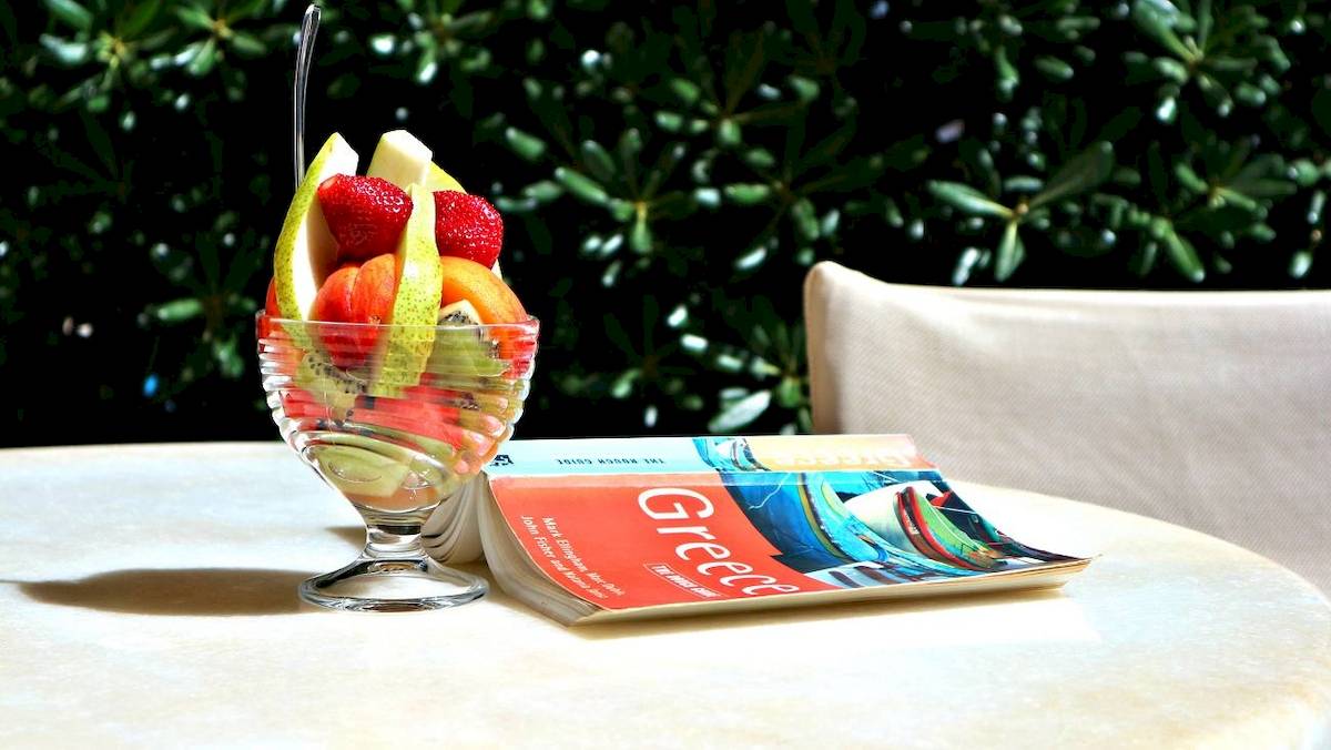 Obstsalat in einem Glas mit einem Buch auf einem Tisch draußen.