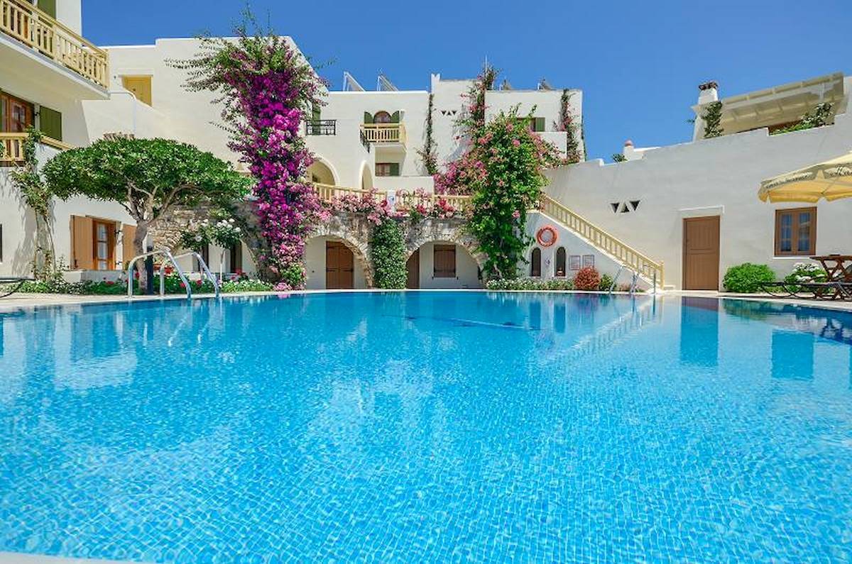 Außenpool des Proteas Hotel & Suites mit weißen Gebäuden und blühenden Pflanzen