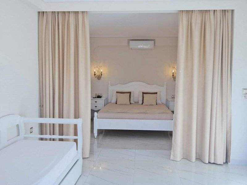 Schlafzimmer im Aegean Palace mit Doppelbett, Nachttischen und großen Vorhängen.