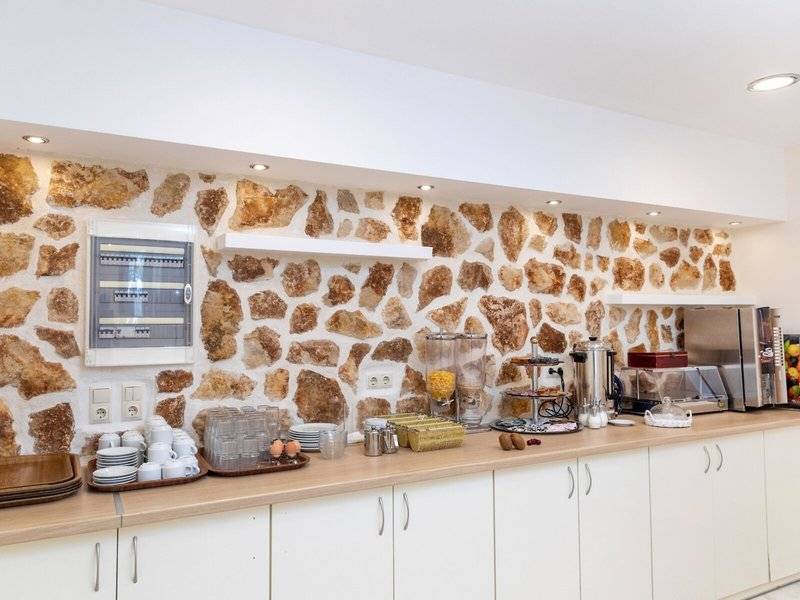 Frühstücksbereich im Hotel Golden Coast mit Steinwand, Frühstücksbuffet und Kaffeemaschine.